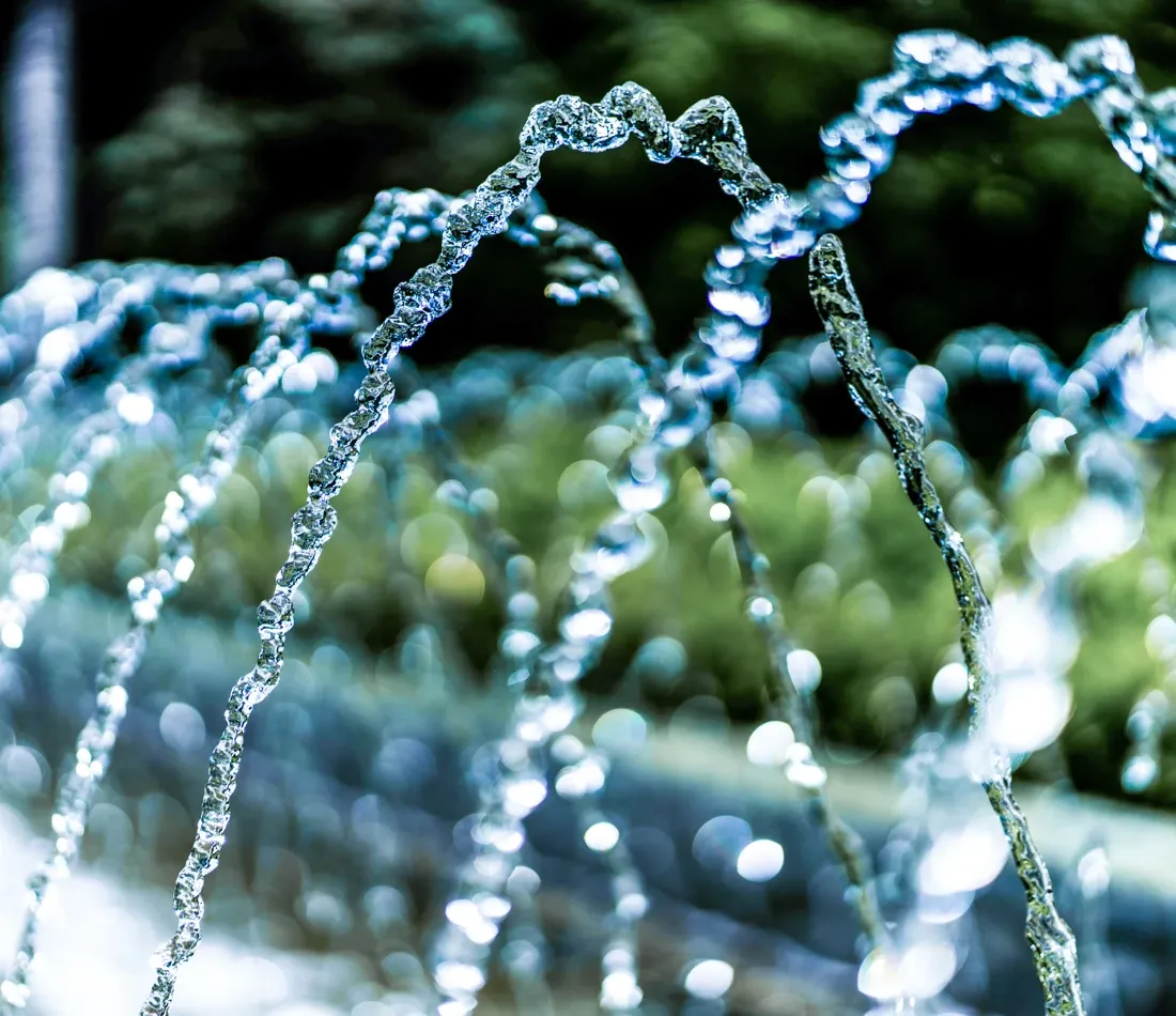 Getti d’acqua di una fontana davanti a vegetazione sfocata