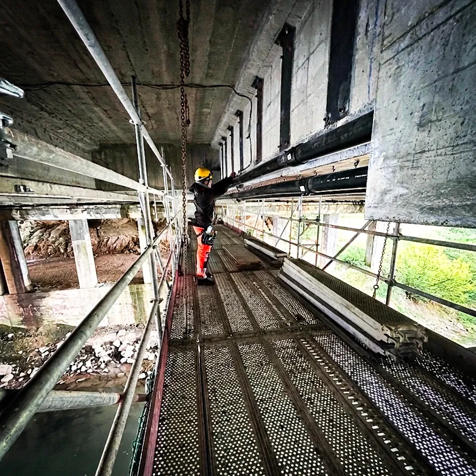Tecnico con casco su una passerella di ponteggio sotto l’impalcato di un ponte