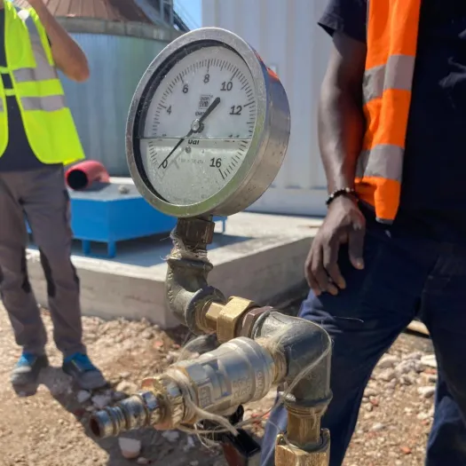 Manometro montato su un raccordo di una tubazione in cantiere, tra due operatori in gilet ad alta visibilità